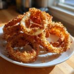 A pile of golden brown, crispy Air Fryer Onion Rings stacked on a small white plate near a sunny window.