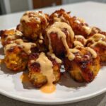 Close-up of crispy Air Fryer Salmon Bites generously drizzled with creamy Bang Bang Sauce on a white plate.
