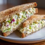Close-up of an Avocado Egg Salad Sandwich cut in half, showing creamy filling with avocado chunks and red onion on toasted bread.