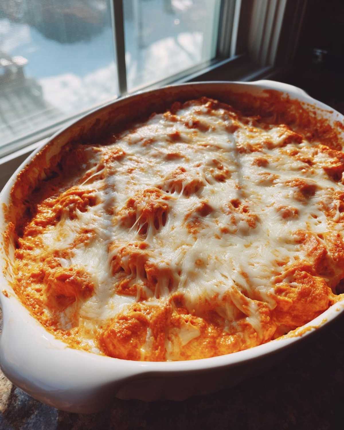 Close-up of a bubbling, orange Baked Buffalo Chicken Dip topped with melted, stringy mozzarella cheese.