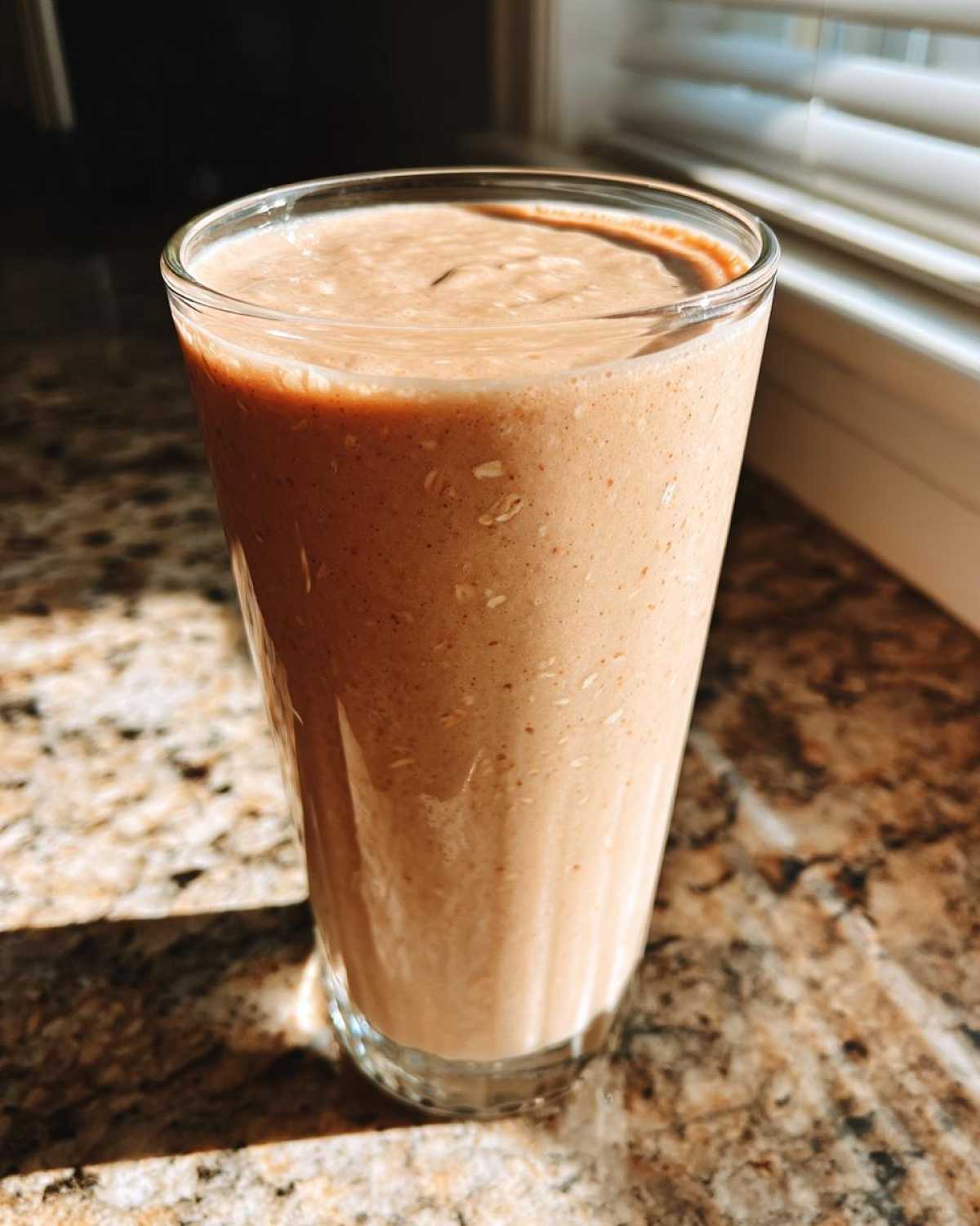 A thick, creamy Banana Peanut Butter Smoothie served in a tall glass on a granite countertop.