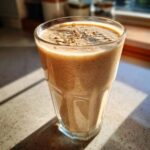 A tall glass filled with a thick Banana Peanut Butter Smoothie, topped with rolled oats.