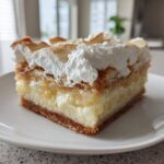 A thick slice of Banana Pudding Cheesecake Bars featuring a creamy filling, crust, and topped with meringue and whipped cream.