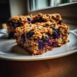 A close-up, appetizing shot of a square piece of Blueberry Baked Oatmeal Squares showing oats and juicy blueberries.