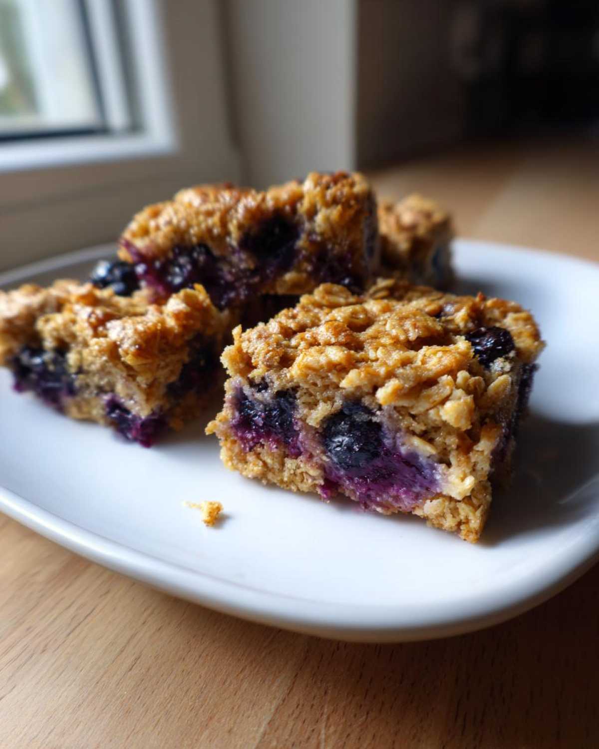 Four rich, golden-brown Blueberry Baked Oatmeal Squares with visible whole blueberries, served on a white plate.