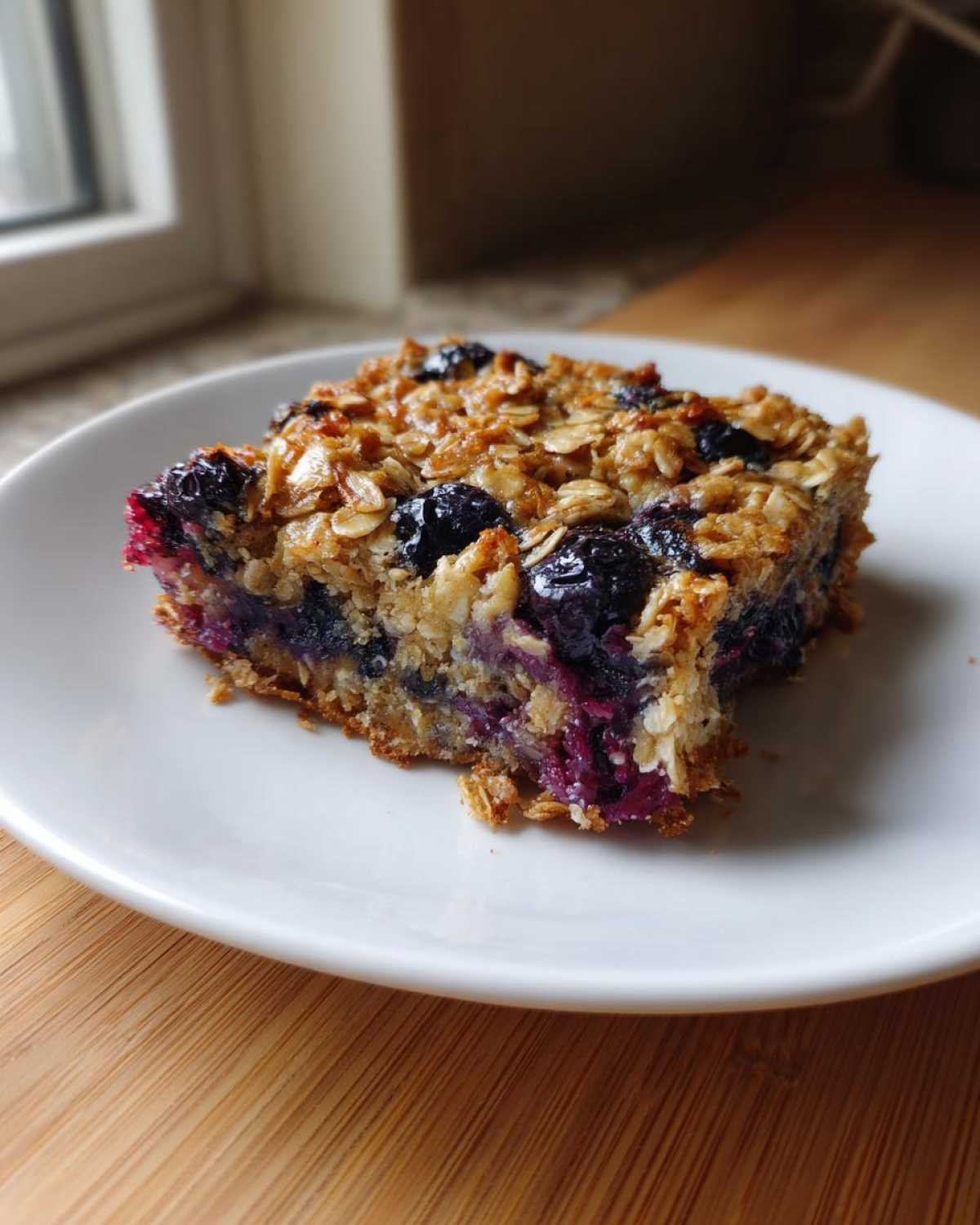 A single serving of moist Blueberry Baked Oatmeal Squares on a white plate.