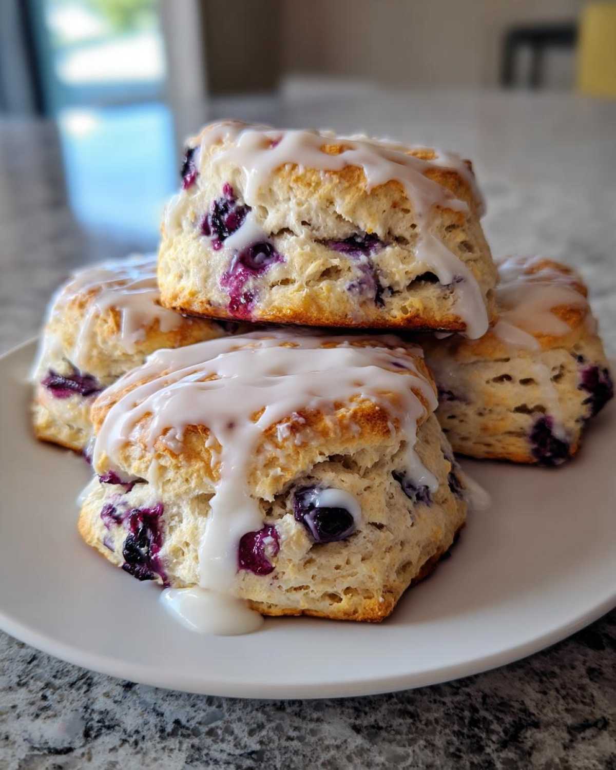 A stack of four freshly baked Blueberry Lemon Scones topped with a thick lemon glaze.