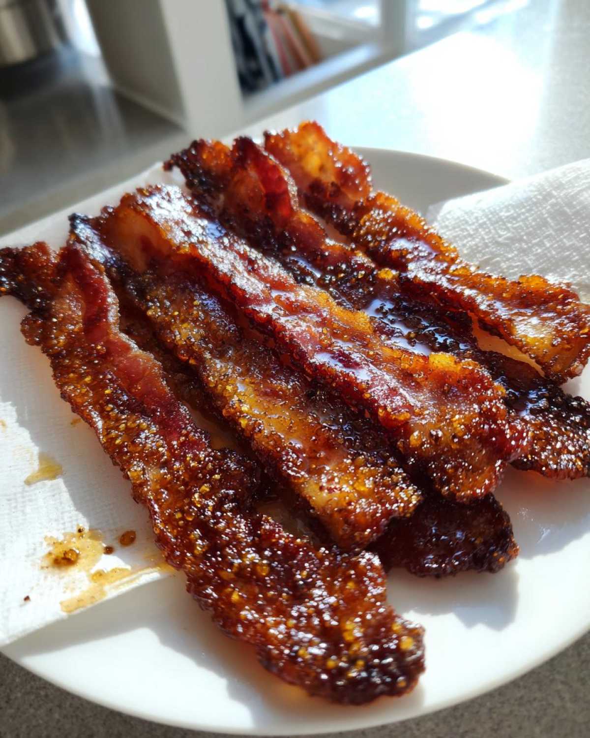 Several crispy strips of Brown Sugar Glazed Bacon glistening with a sweet, caramelized coating on a white plate.