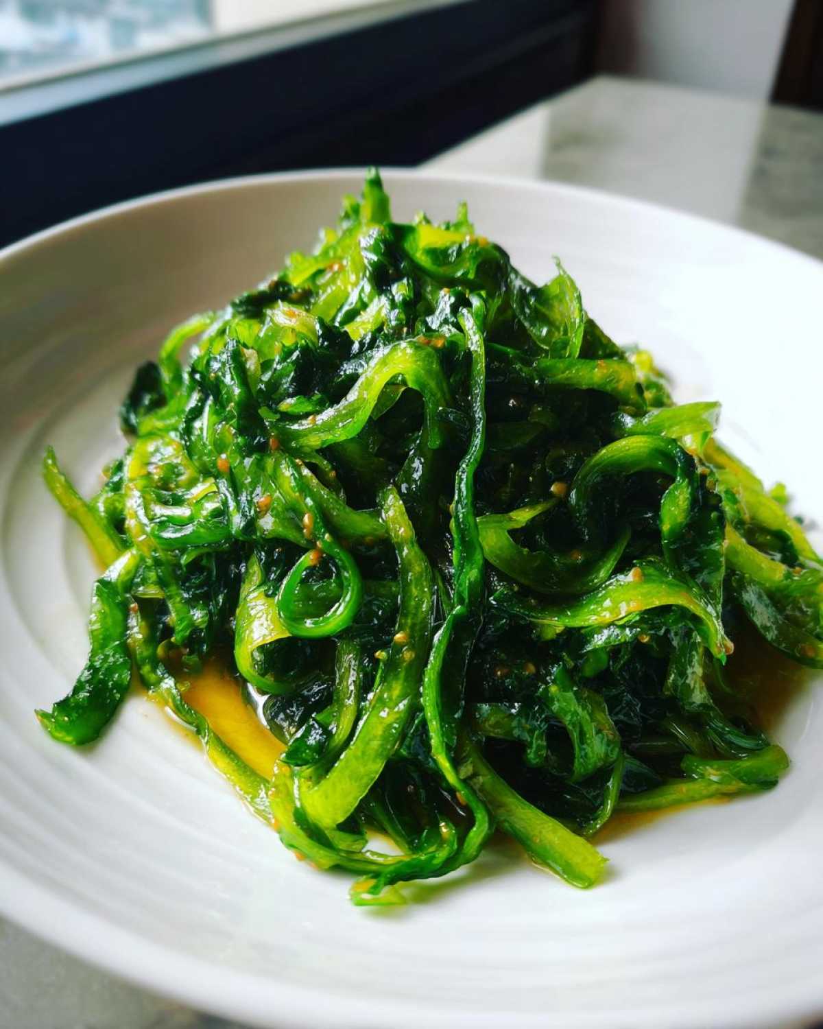 Close-up of bright green, thinly sliced Cabbage Stir Fry with Garlic Ginger Sauce on a white plate.