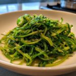 Close-up of vibrant green, thinly sliced cabbage stir fry coated in a glossy garlic ginger sauce.