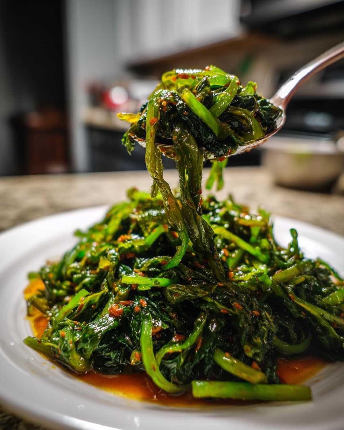 A spoonful of vibrant green Cabbage Stir Fry with Garlic Ginger Sauce being lifted from a white plate.