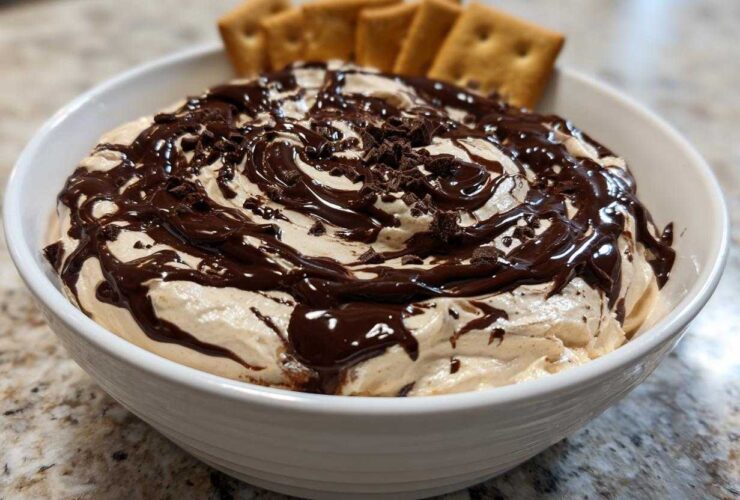 A white bowl filled with creamy Chocolate Peanut Butter Cheesecake Dip, drizzled with fudge and topped with chocolate shavings, served with crackers.