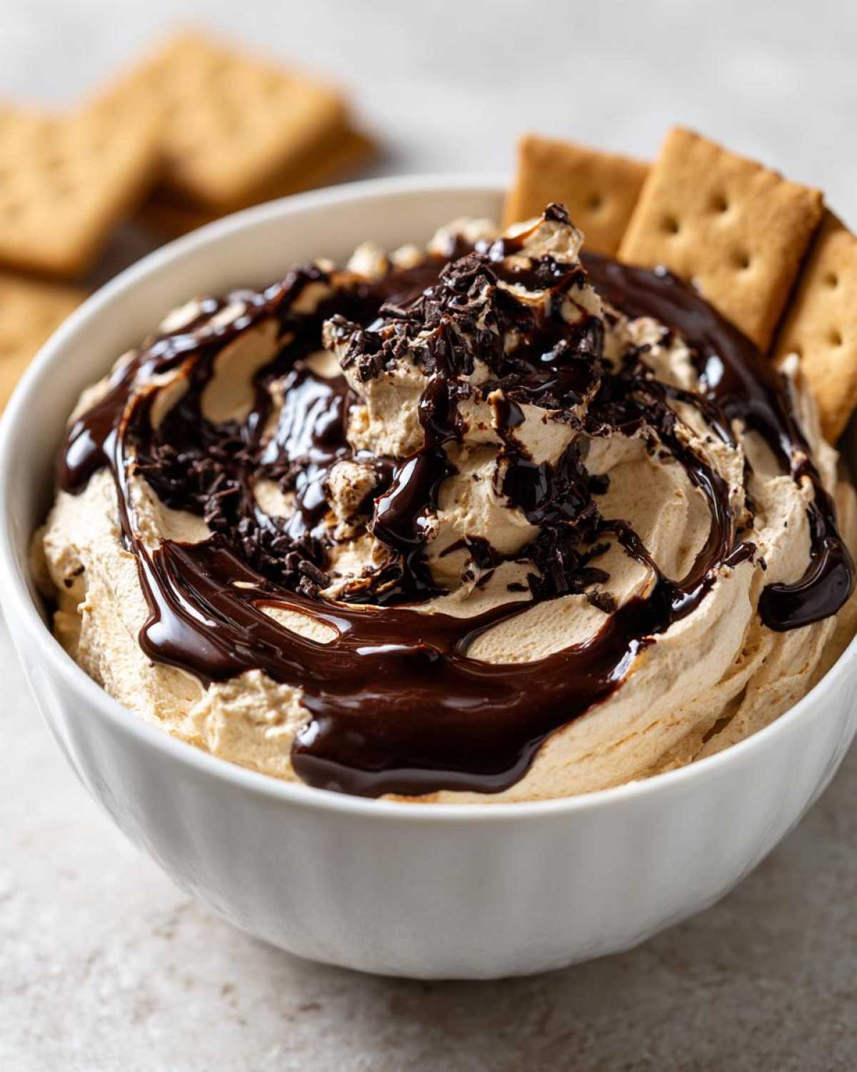 A close-up of rich Chocolate Peanut Butter Cheesecake Dip topped with chocolate syrup and sprinkles, served with graham crackers.