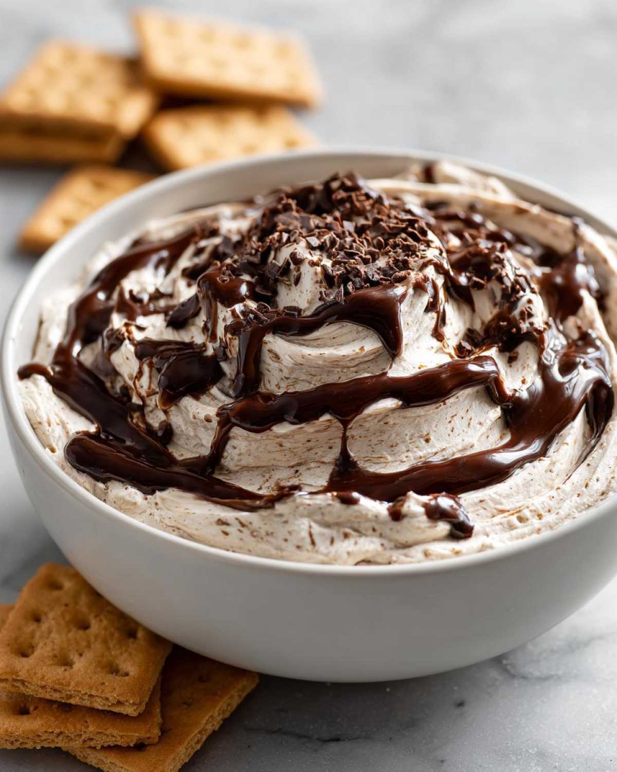 Close-up of a white bowl filled with creamy Chocolate Peanut Butter Cheesecake Dip, drizzled with chocolate sauce and topped with shavings.
