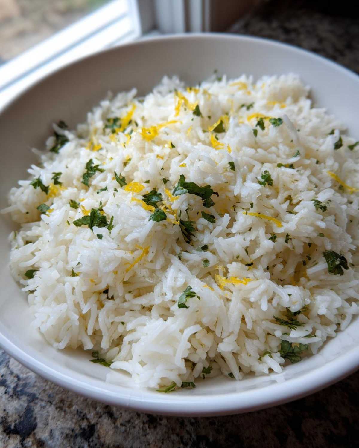 Close-up of fluffy Cilantro Lime Rice garnished with chopped cilantro and bright yellow lime zest in a white bowl.
