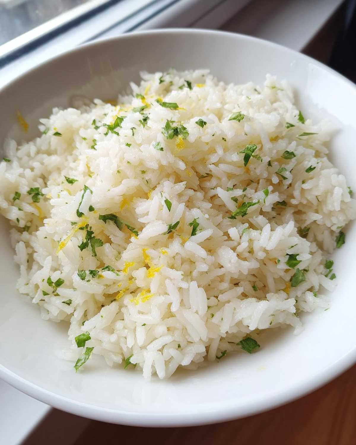 Close-up of fluffy Cilantro Lime Rice topped with chopped cilantro and bright yellow lime zest in a white bowl.