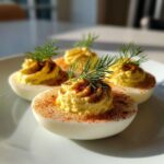 Four halves of Classic Deviled Eggs with Dill Pickle Relish, piped filling, paprika, and fresh dill sprigs on a white plate.