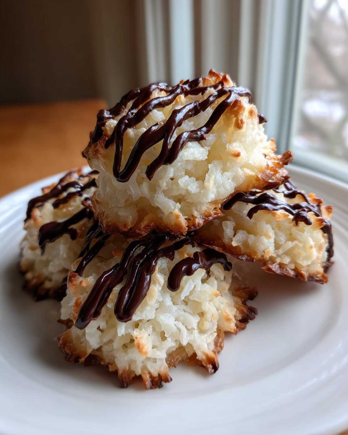 A stack of three golden-edged Coconut Macaroons with Dark Chocolate Drizzle on a white plate.