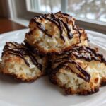 Three golden-brown Coconut Macaroons with Dark Chocolate Drizzle stacked on a white plate.