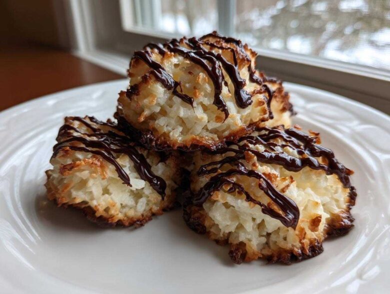 Three golden-brown Coconut Macaroons with Dark Chocolate Drizzle stacked on a white plate.