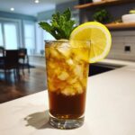Tall glass filled with ice, dark brown liquid, and topped with mint and a lemon slice, showcasing Cold Brew Lemonade.