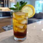 A tall glass filled with ice, dark brown Cold Brew Lemonade, garnished with a lemon slice and mint sprig.