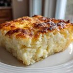 A close-up of a square serving of Copycat Cracker Barrel Hashbrown Casserole with a golden-brown, cheesy top.