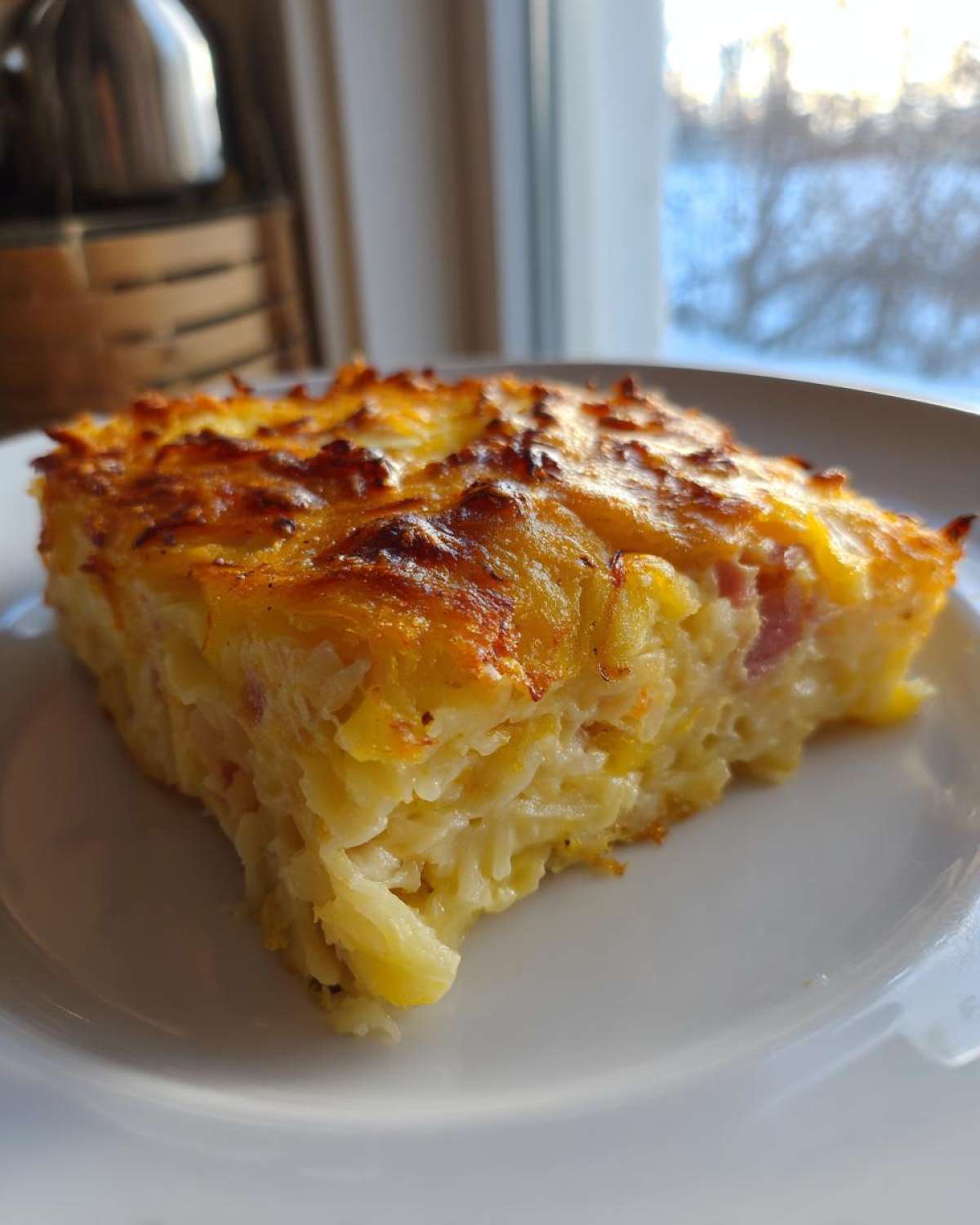 A golden-brown slice of creamy Copycat Cracker Barrel Hashbrown Casserole served on a white plate.