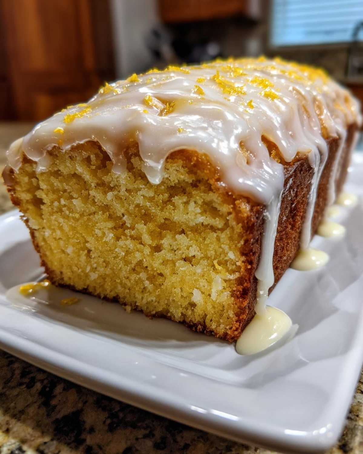 A close-up of a freshly baked Copycat Starbucks Iced Lemon Loaf with thick white glaze dripping down the sides and lemon zest on top.