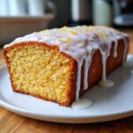 A close-up of a moist slice of Copycat Starbucks Iced Lemon Loaf topped with thick, dripping lemon glaze and zest.