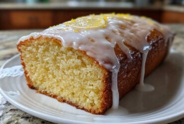 A moist slice of Copycat Starbucks Iced Lemon Loaf, topped with thick white glaze and lemon zest.