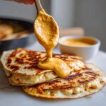 A spoonful of thick, orange Copycat Taco Bell Chicken Quesadilla Sauce is drizzled over stacked, grilled cheese quesadillas.