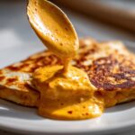 A spoonful of creamy orange Copycat Taco Bell Chicken Quesadilla Sauce being poured over a grilled quesadilla slice.