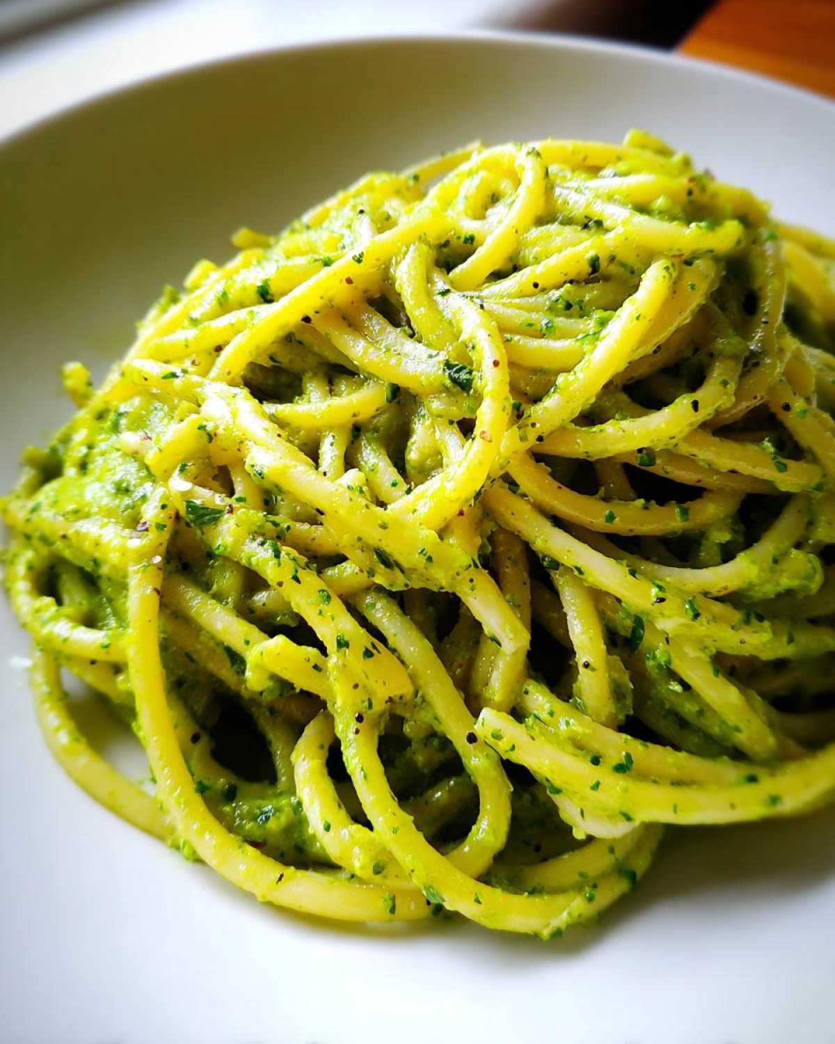 A close-up shot of thick spaghetti coated in vibrant green Creamy Avocado Pasta sauce served on a white bowl.