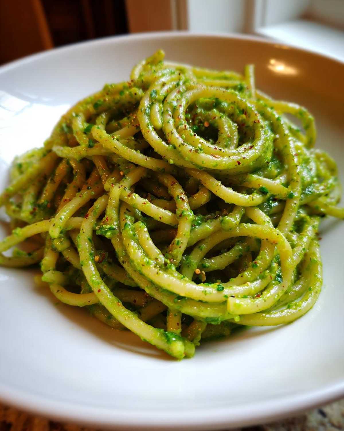 A close-up shot of thick pasta noodles coated in vibrant green Creamy Avocado Pasta sauce, served in a white bowl.