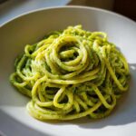 A close-up shot of spaghetti tossed in bright green Creamy Avocado Pasta sauce, beautifully swirled in a white bowl.