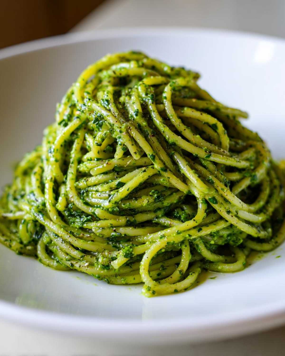 A vibrant mound of spaghetti coated in bright green Creamy Avocado Pasta sauce served in a white bowl.