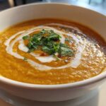Close-up of a bowl of vibrant orange Creamy Coconut Lentil Soup, swirled with coconut cream and topped with fresh cilantro.