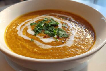 Close-up of a bowl of vibrant orange Creamy Coconut Lentil Soup, swirled with coconut cream and topped with fresh cilantro.