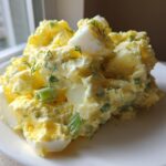 A generous mound of Creamy Dill Potato Salad mixed with chopped eggs and green onions on a white plate.