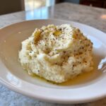 A mound of fluffy Creamy Garlic Mashed Cauliflower topped with cracked pepper and melted butter.
