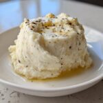 A serving of fluffy Creamy Garlic Mashed Cauliflower topped with melted butter and black pepper.
