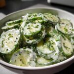 Close-up of thinly sliced cucumbers coated in a creamy dressing and topped with fresh dill and chives in a white bowl, featuring Creamy German Cucumber Salad.