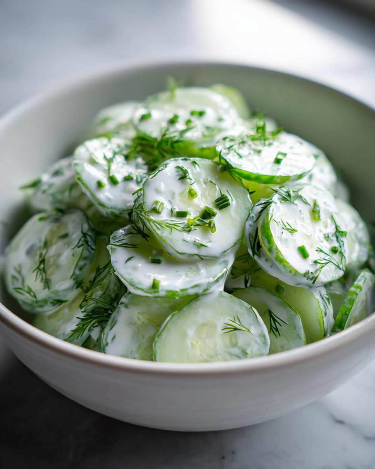 Close-up of thinly sliced cucumbers tossed in a creamy dressing and topped with fresh dill and chives, featuring Creamy German Cucumber Salad.