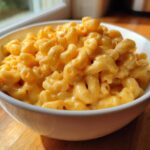 A close-up of creamy, cheesy Instant Pot Mac and Cheese served in a white bowl on a wooden surface.