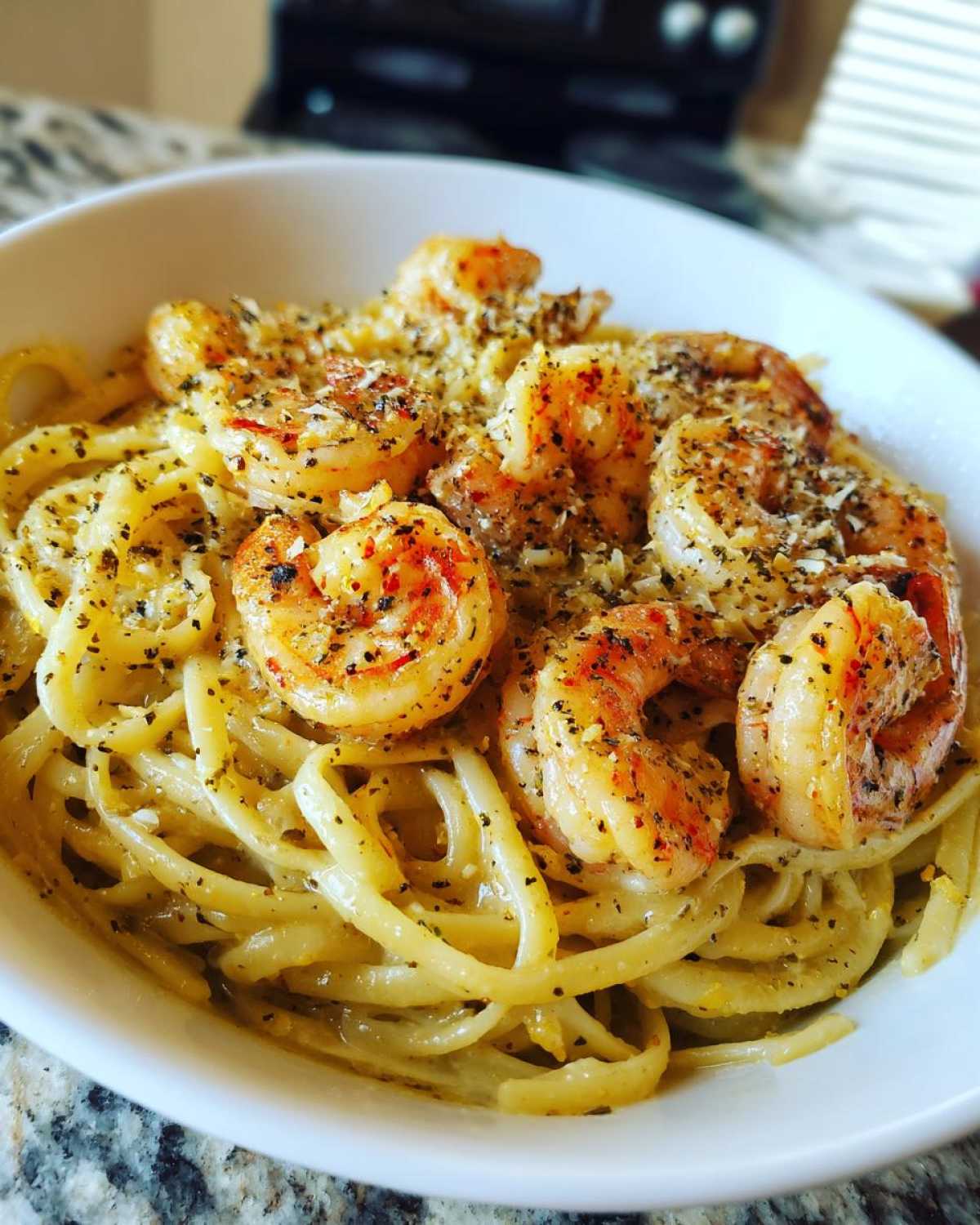 A close-up photo of a white bowl filled with Creamy Lemon Garlic Shrimp Pasta, topped with seasoned shrimp and grated cheese.