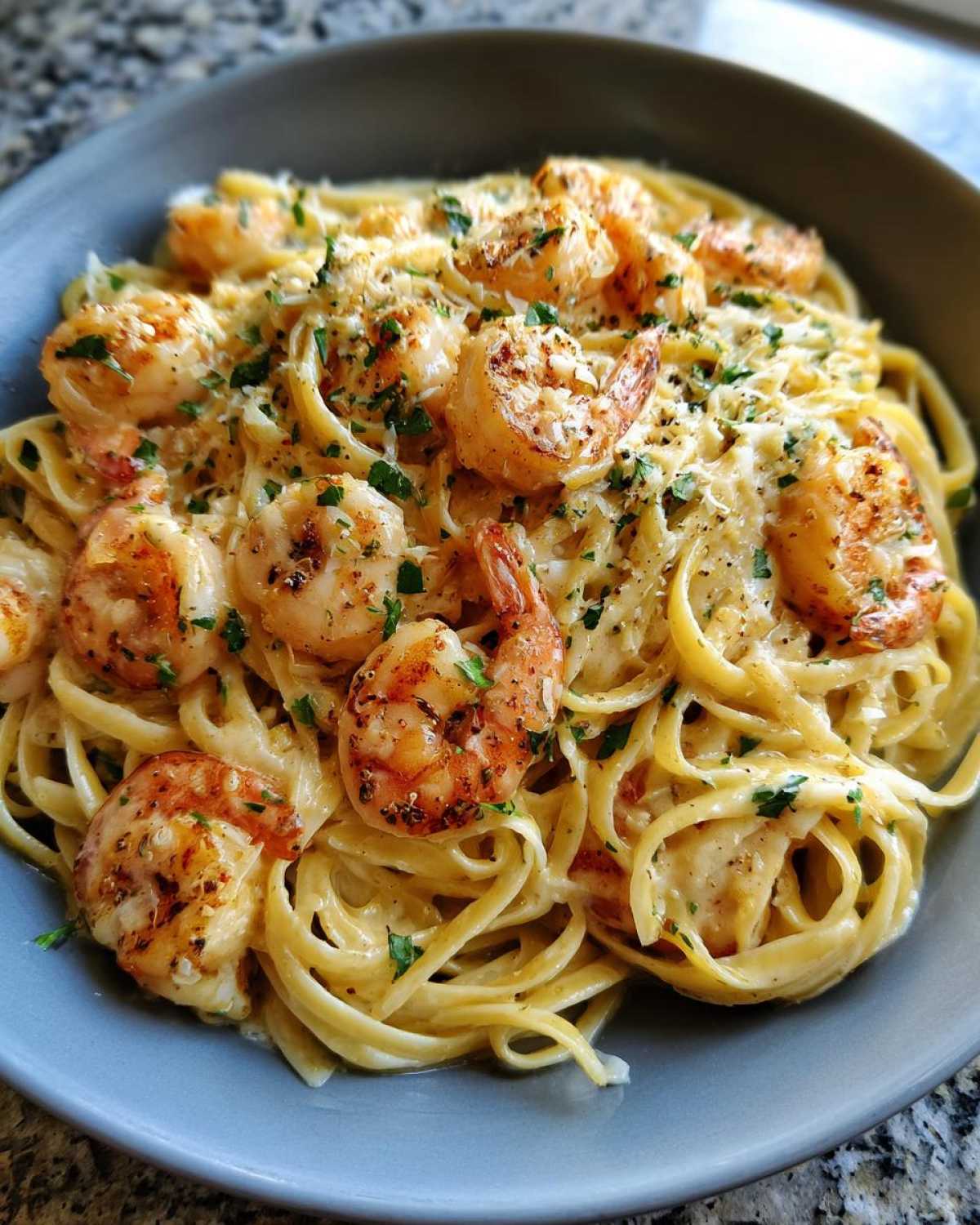 Close-up of a bowl filled with Creamy Lemon Garlic Shrimp Pasta, topped with grilled shrimp and parsley.