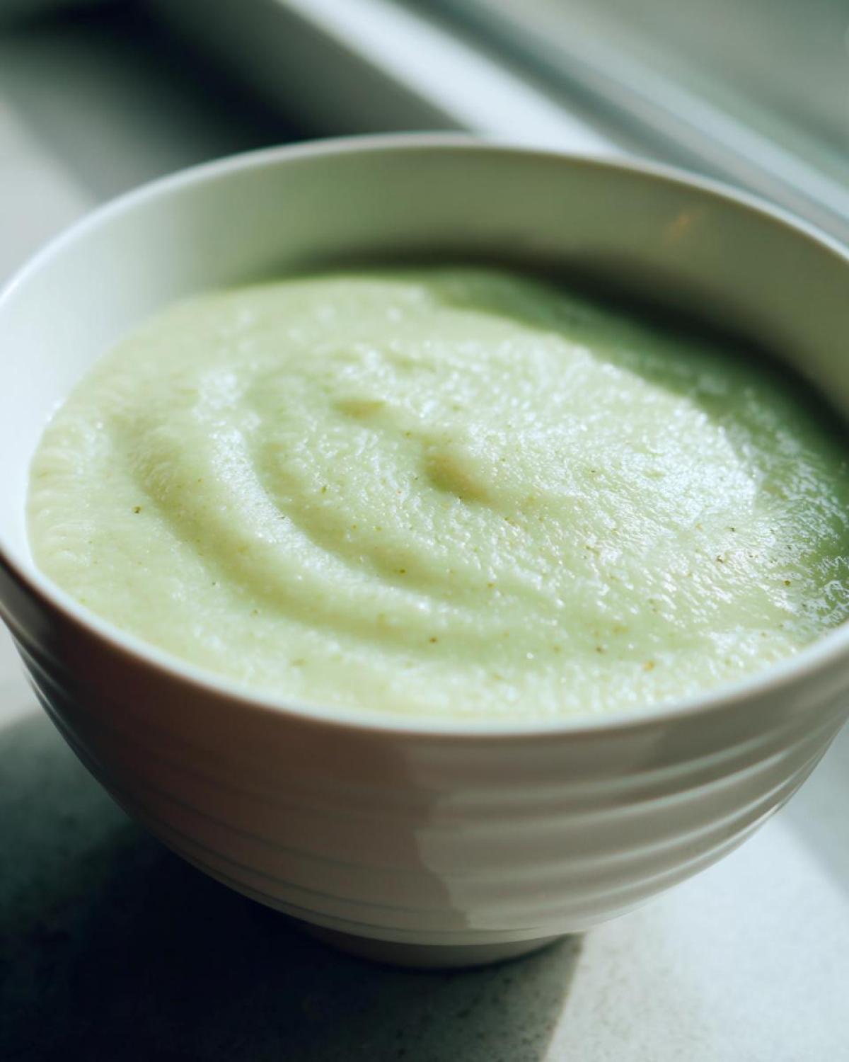 A close-up, slightly moody shot of thick, pale green Creamy Potato Leek Soup served in a white bowl.