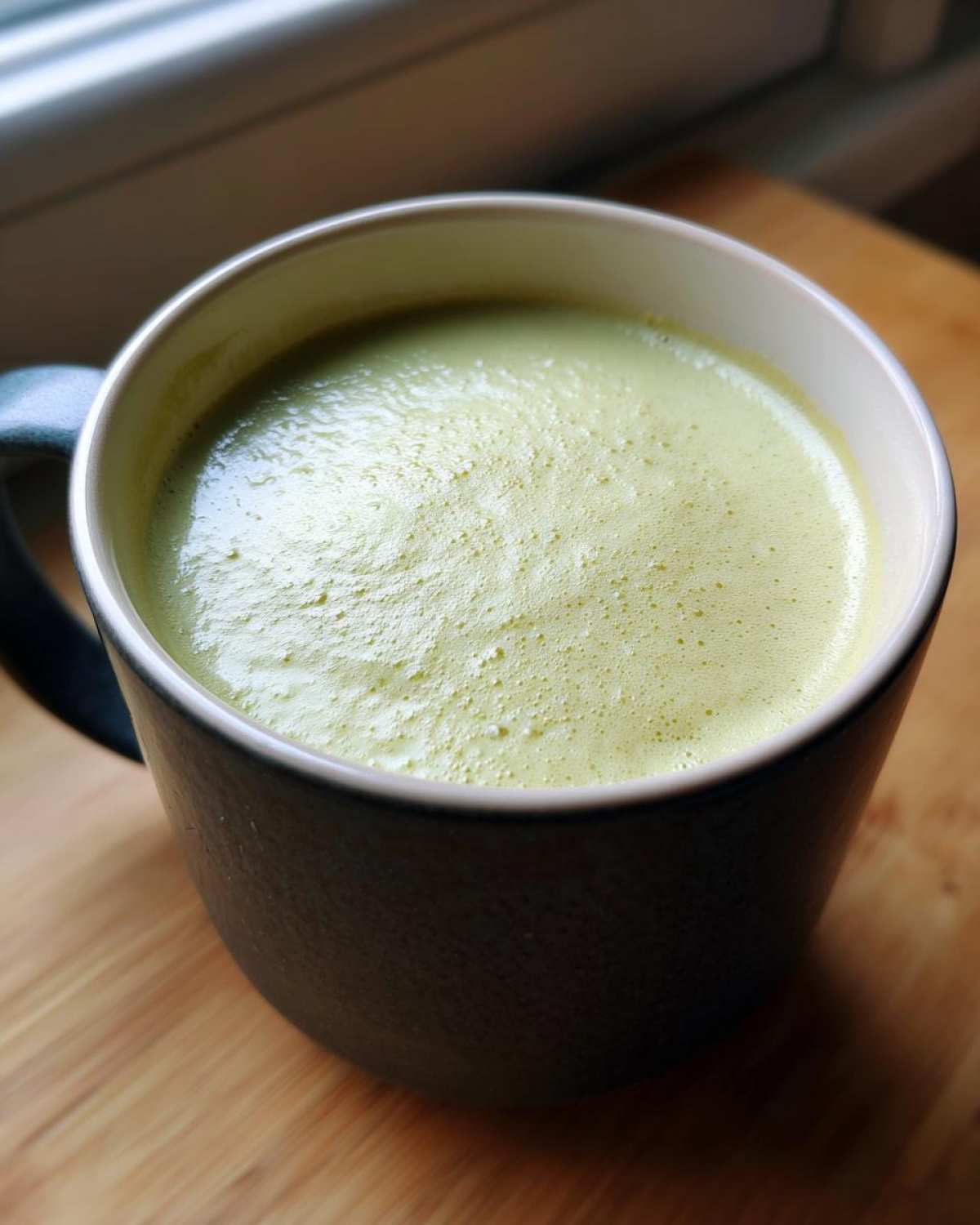 Close-up of a bowl of creamy Potato Leek Soup with a light green hue and foamy top.