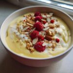 Close-up of a Creamy Vanilla Protein Smoothie Bowl topped with raspberries, granola, and sliced almonds.